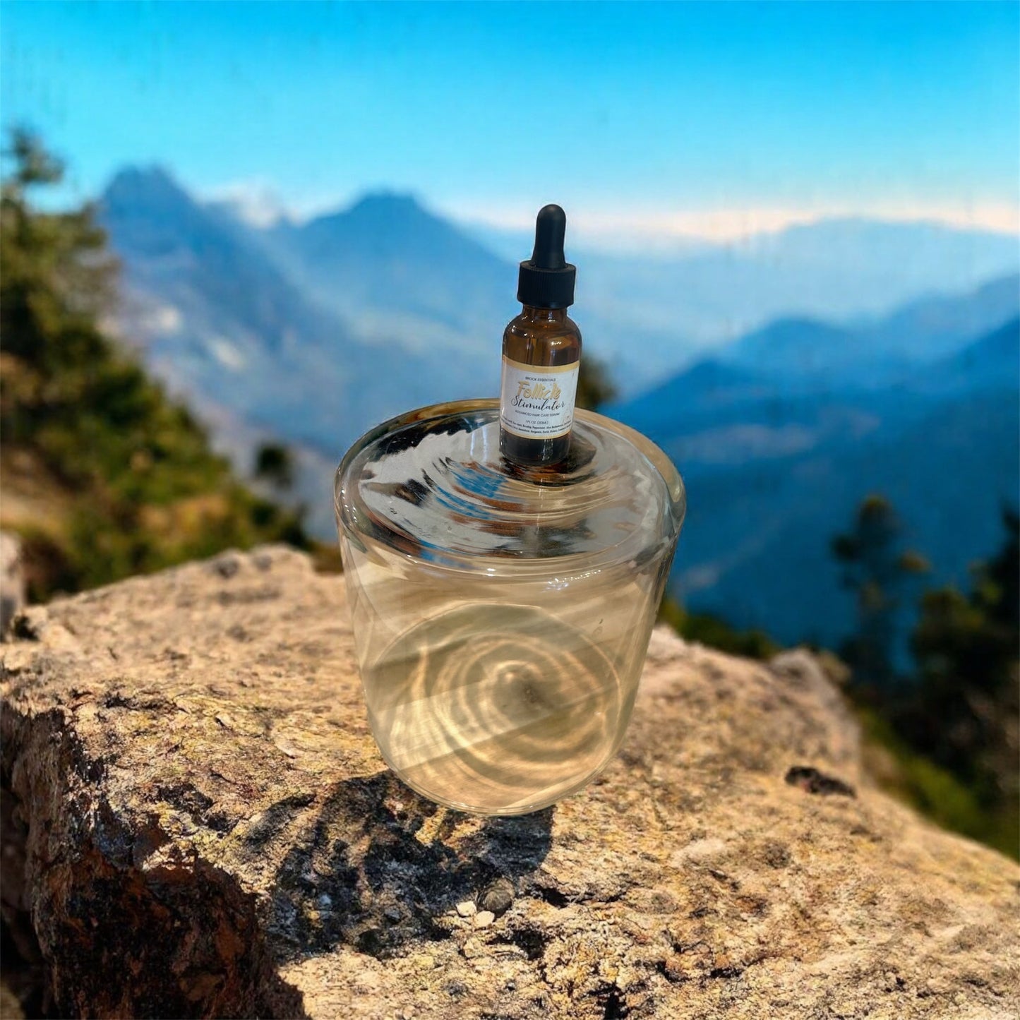 Brock Essentials hair follicle stimulator serum bottle on a glass stand against a scenic mountain landscape